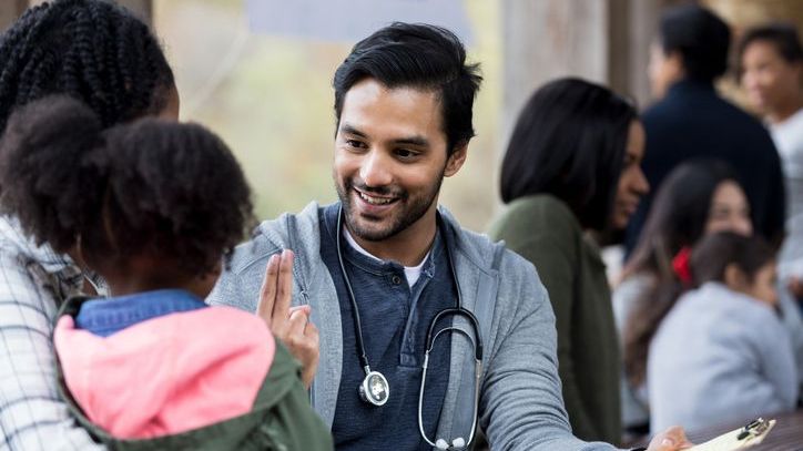 A doctor who works for a nonprofit organization interacts with a mother and daughter during an outreach event.