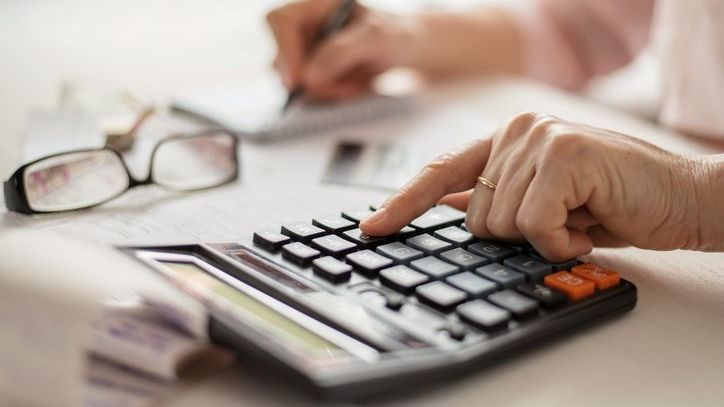 A woman adds up her living expenses on a calculator while constructing her monthly budget.